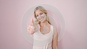 Young blonde woman smiling with thumb up over isolated pink background