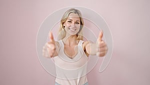 Young blonde woman smiling with thumbs up over isolated pink background