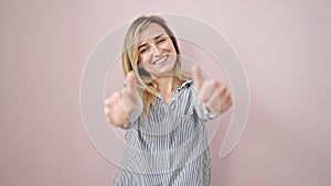 Young blonde woman smiling with thumbs up over isolated pink background