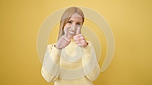 Young blonde woman smiling with thumbs up over isolated yellow background