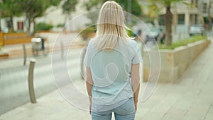 Young blonde woman standing on back view at street