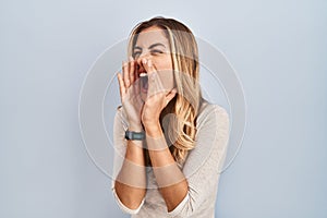 Young blonde woman standing over isolated background shouting angry out loud with hands over mouth