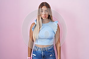 Young blonde woman standing over pink background depressed and worry for distress, crying angry and afraid