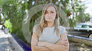 Young blonde woman standing with serious expression and arms crossed gesture at park