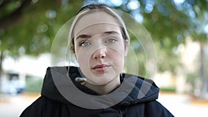 Young blonde woman standing with serious expression at park