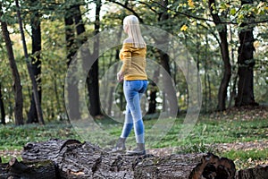 Young blonde woman standing on a tree branch in the forest