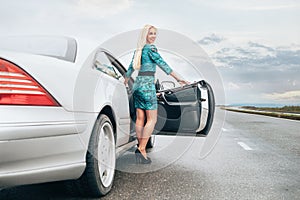 Young blonde woman stay near car on lonely highway