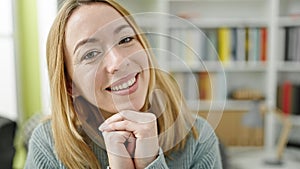 Young blonde woman student sitting on table smiling at library university