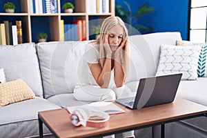 Young blonde woman student stressed sitting on sofa studying at home