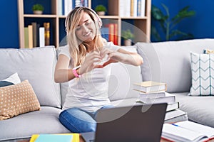 Young blonde woman studying using computer laptop at home smiling in love doing heart symbol shape with hands