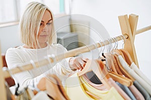 Young blonde woman stylist seller chooses clothes on hanger in bright studio