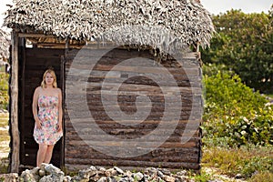 Young blonde woman in summer dress near old wooden house at the beach photo