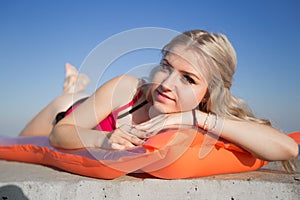 Young blonde woman sunbathes on pool raft looking at camera