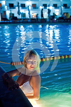 Young blonde woman in swimming pool bathing at night