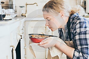 Young blonde woman taking heart shaped cake out of the oven