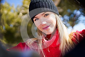 Young blonde woman taking a selfie in a snowy mountain forest in winter.