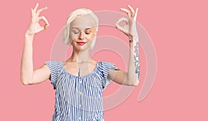 Young blonde woman with tattoo wearing casual clothes relax and smiling with eyes closed doing meditation gesture with fingers