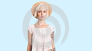 Young blonde woman with tattoo wearing summer hat relaxed with serious expression on face