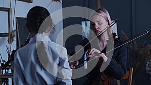 Young blonde woman teaching a little girl student how to properly hold a bow while playing violin