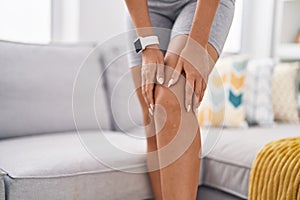 Young blonde woman touching knee for injury at home