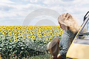 Young blonde woman travelling by campervan. Overlooking sunflower field on sunny summer day