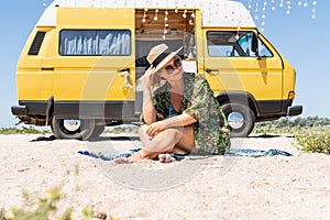 Young blonde woman travelling by vintage campervan at the seaside. Relaxing on the beach