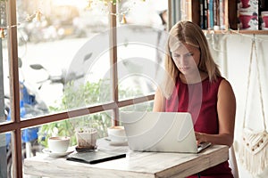 Young blonde woman typing in laptop in cafe