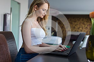 Young blonde woman typing on laptop indoors