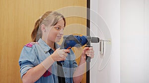 Young blonde woman using hand drill indoors. Concept of women independence, feminism, gender equality, repair and