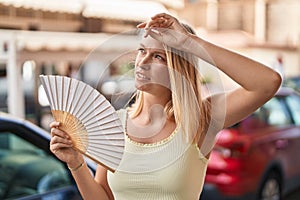 Young blonde woman using handfan at street