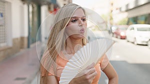 Young blonde woman using handfan suffering for hot at street