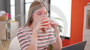 Young blonde woman using laptop drinking coffee at dinning room