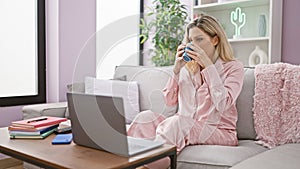 Young blonde woman using laptop drinking coffee at home