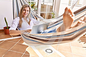 Young blonde woman using laptop lying on hammock at terrace