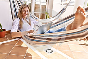 Young blonde woman using laptop lying on hammock at terrace