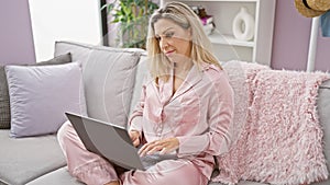 Young blonde woman using laptop with serious face at home