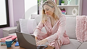 Young blonde woman using laptop with serious face at home