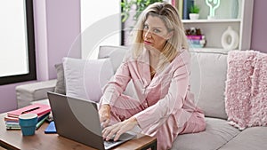 Young blonde woman using laptop with serious face pointing at home