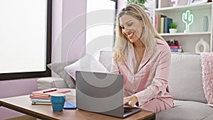 Young blonde woman using laptop sitting on sofa smiling at home