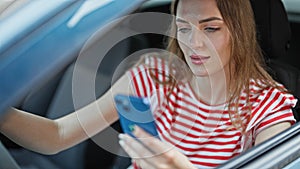 Young blonde woman using smartphone driving car at street