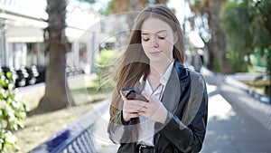 Young blonde woman using smartphone with serious expression at park