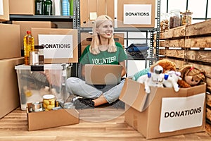 Young blonde woman volunteer using laptop sitting on floor at charity center
