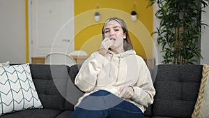Young blonde woman watching movie sitting on sofa at home