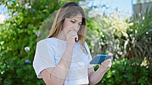 Young blonde woman watching video on smartphone with serious expression at park