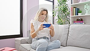 Young blonde woman watching video on smartphone sitting on sofa with serious face at home