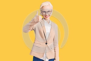 Young blonde woman wearing business clothes and glasses doing happy thumbs up gesture with hand