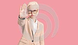 Young blonde woman wearing business clothes and glasses doing stop sing with palm of the hand