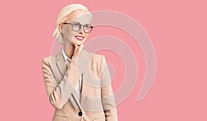 Young blonde woman wearing business clothes and glasses with hand on chin thinking about question, pensive expression