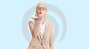 Young blonde woman wearing business clothes and glasses looking at the camera blowing a kiss with hand on air being lovely and