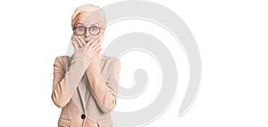 Young blonde woman wearing business clothes and glasses shocked covering mouth with hands for mistake